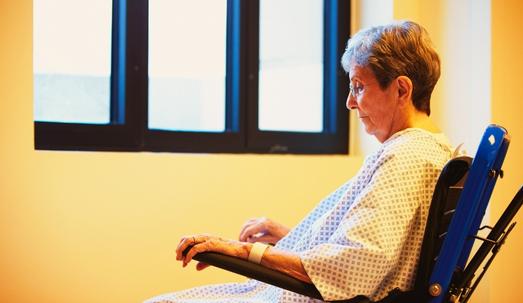 Neglected senior female patient in a nursing home sitting on her wheelchair facing the window