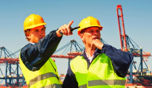 Two male dockers in discussion in front of a large industrial harbor