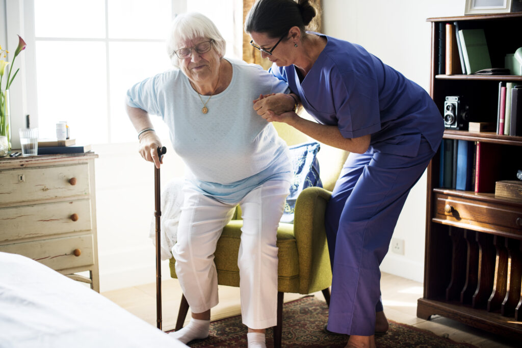 Helthcare workers helping older lady up off chair