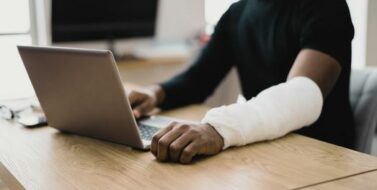 Injured Worker Compensation. Broken Arm African Man On Computer
