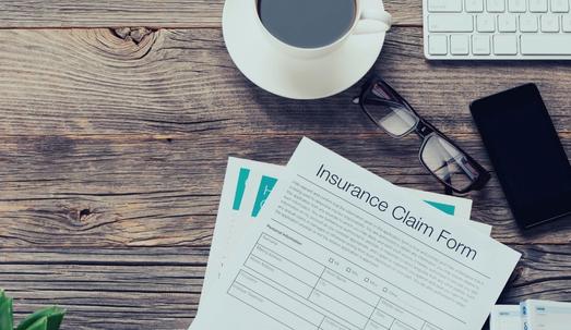 Insurance claim form. The form is on an old wooden table with a mobile phone, coffee, glasses and a keyboard. There is copy space to the right. Accident and insurance concept