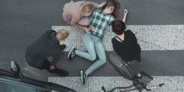 Passersby helping an unconscious casualty of a car accident lying next to the bike. Concept of Who Is Liable for a Hit and Run Accident