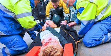 Paramedics and a fireman strapping a wounded woman with a neck brace on a stretcher. Effects of car crash on human body