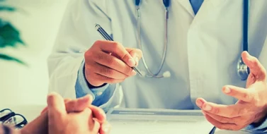 Doctor writing a medical certificate while talking to his patient.