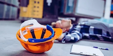 a man lying on the floor of a warehouse, apparently injured or unconscious.