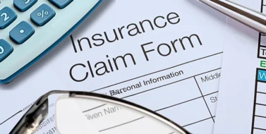 An insurance claim form surrounded by financial documents, a calculator, a pen, and eyeglasses. Ask for More After an Insurance Settlement Offer