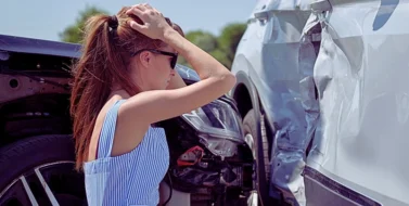 A woman sitting on the roadside, holding her head in distress after a car accident. Why Insurance Companies Delay Car Accident Claims